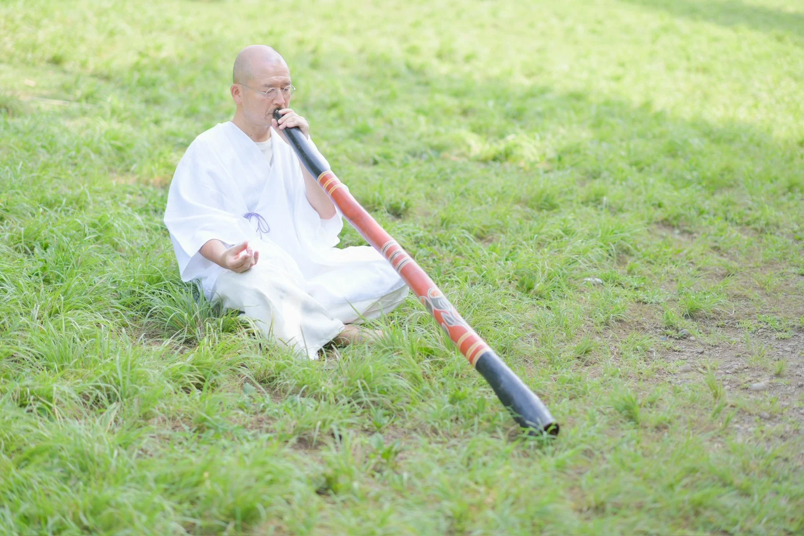 緑の中で座ってディジュリドゥを奏でる地球人てらじん